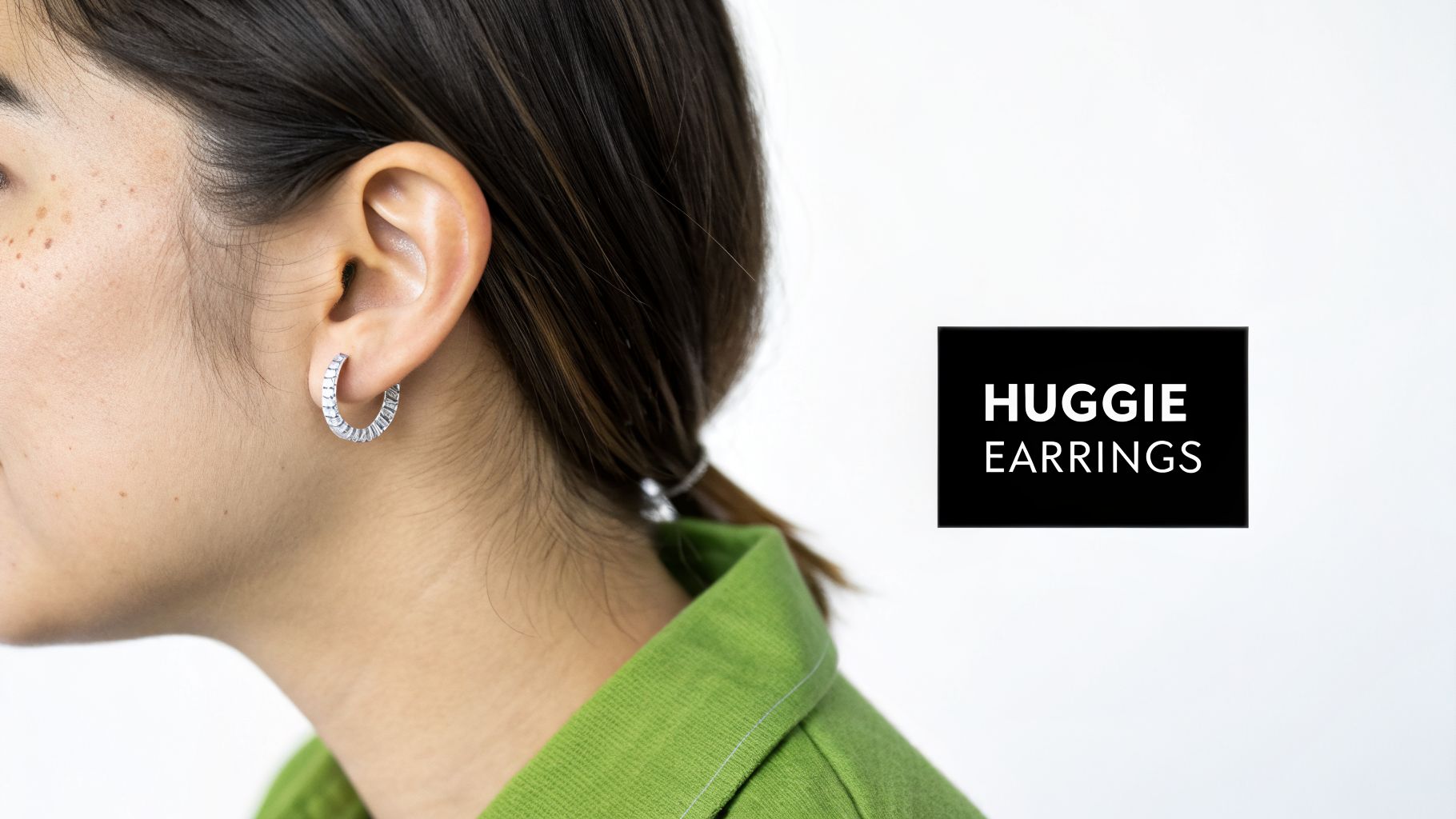 Close-up of a person's ear wearing a silver huggie hoop earring with baguette stones.