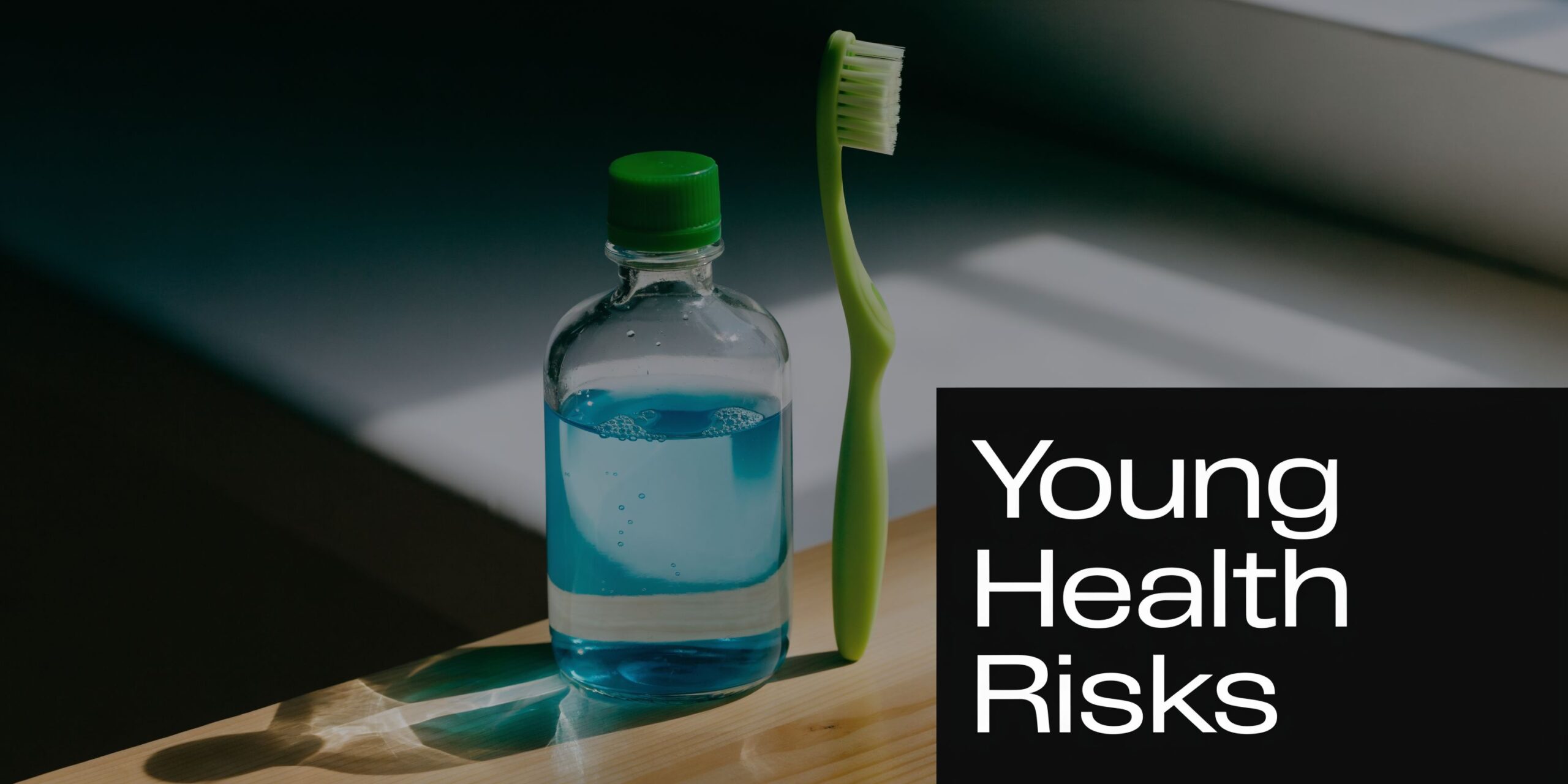 A green toothbrush and a glass bottle of blue mouthwash resting on a wooden surface.