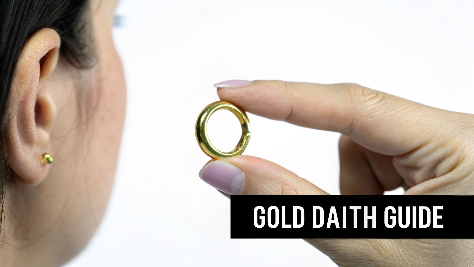 A close-up of a person's ear with a gold stud earring, and a hand holding a gold daith ring.