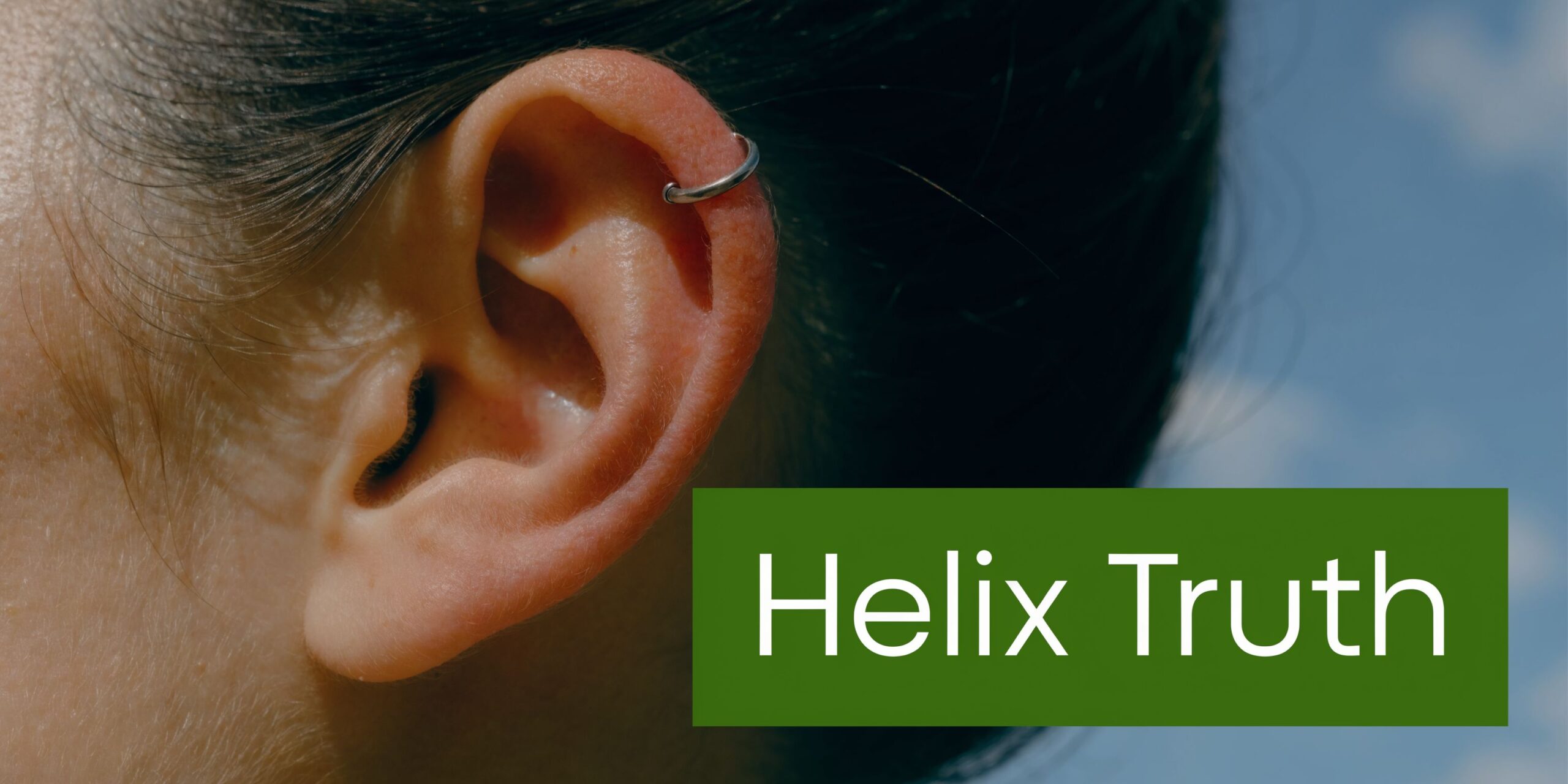 A close up view of a person's ear featuring a minimalist silver hoop helix piercing.