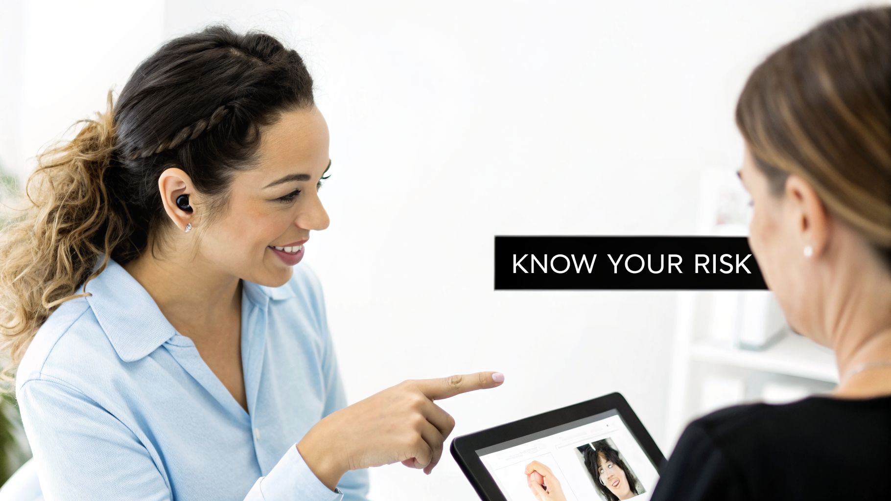 A smiling woman with an earbud points at a tablet while consulting another woman, discussing health risks.
