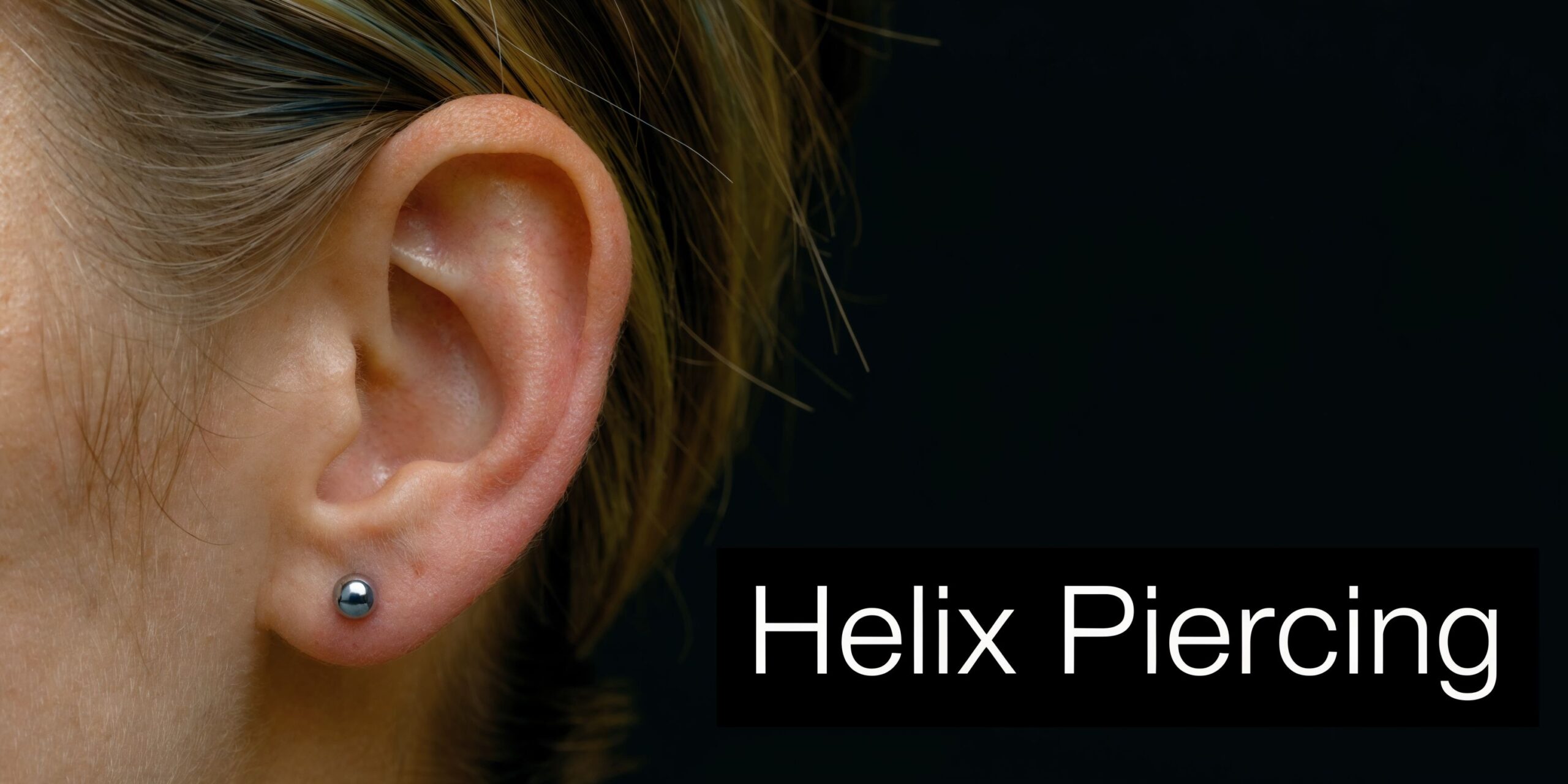 A close-up view of an ear lobe piercing with a small metallic ball earring on a person.