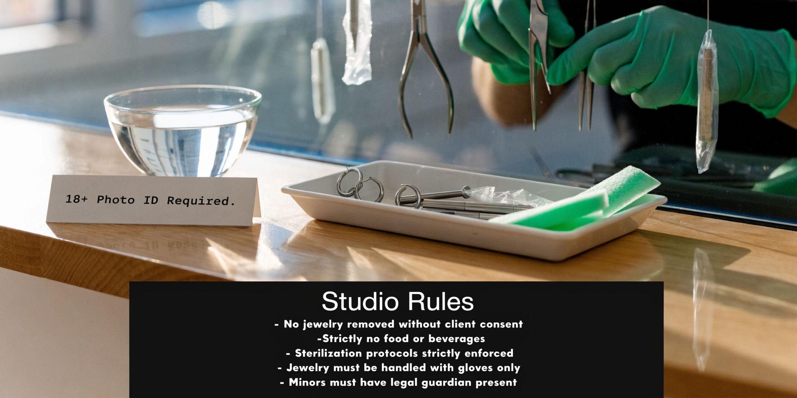 A professional piercer in gloves organizes tools in a clean studio with an age requirement notice.