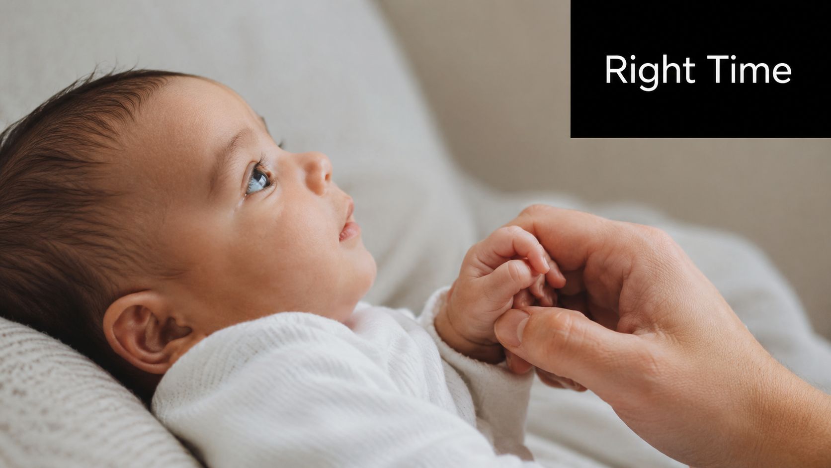 A close-up view of an adorable baby lying down while holding a parent's hand gently.