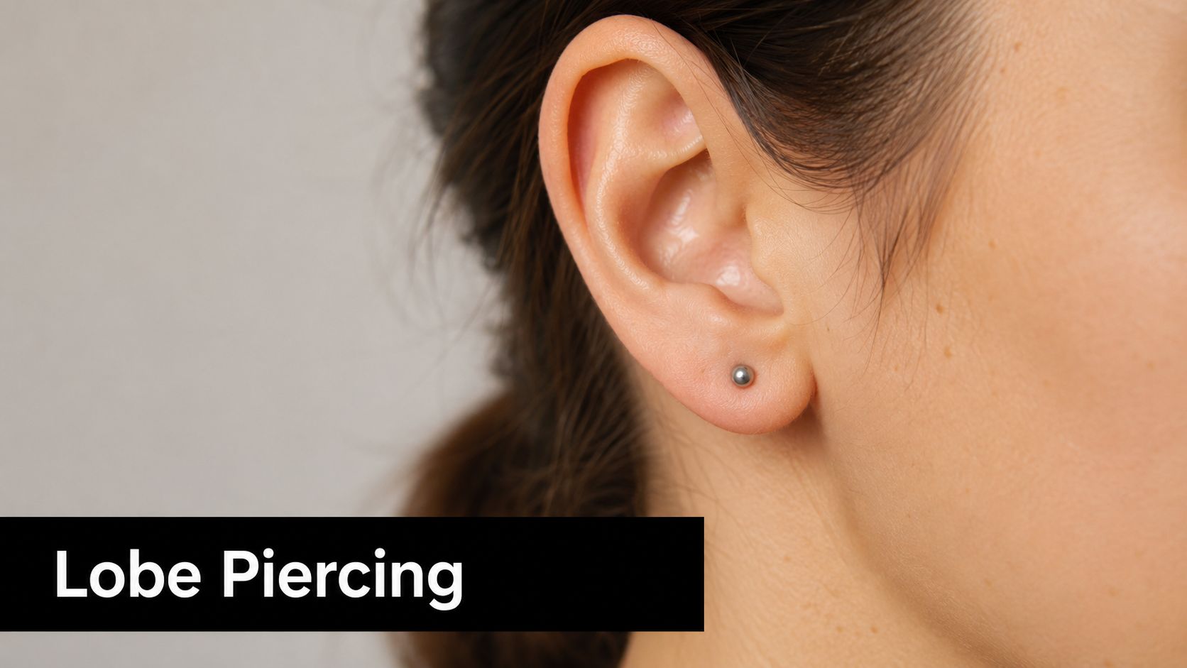 A close-up view of a woman's earlobe showing a simple, elegant metallic ball stud earring.