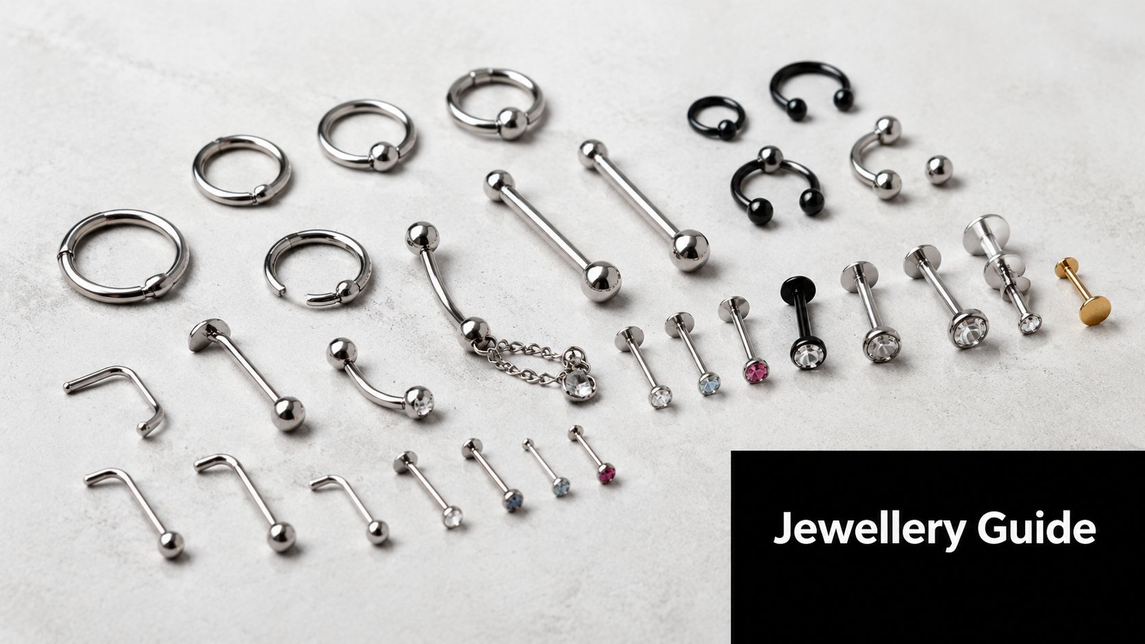 An assortment of various metal body piercing jewelry laid out on a light grey textured background.