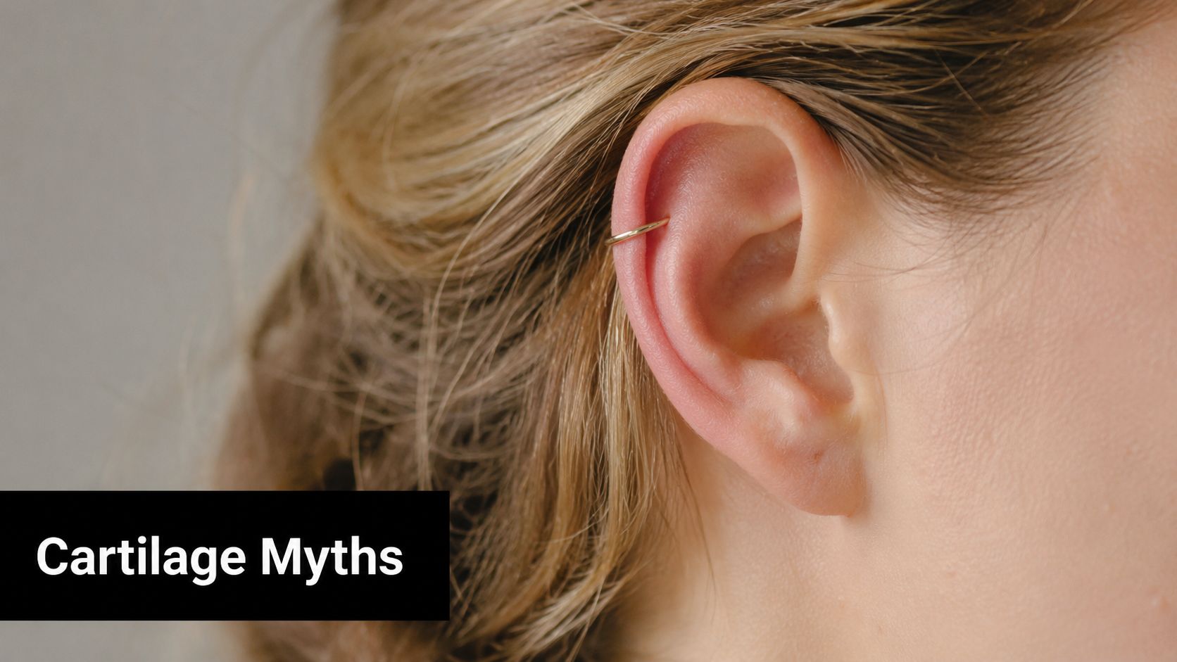 A close-up view of a woman's ear featuring a simple gold hoop cartilage piercing.
