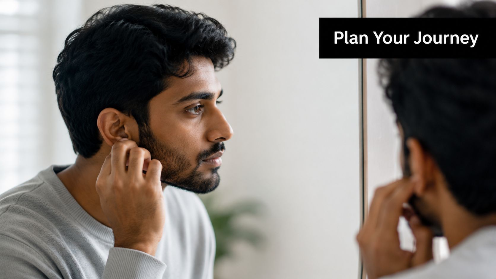 A young man with dark hair adjusting his ear earring while looking at his reflection in the mirror.