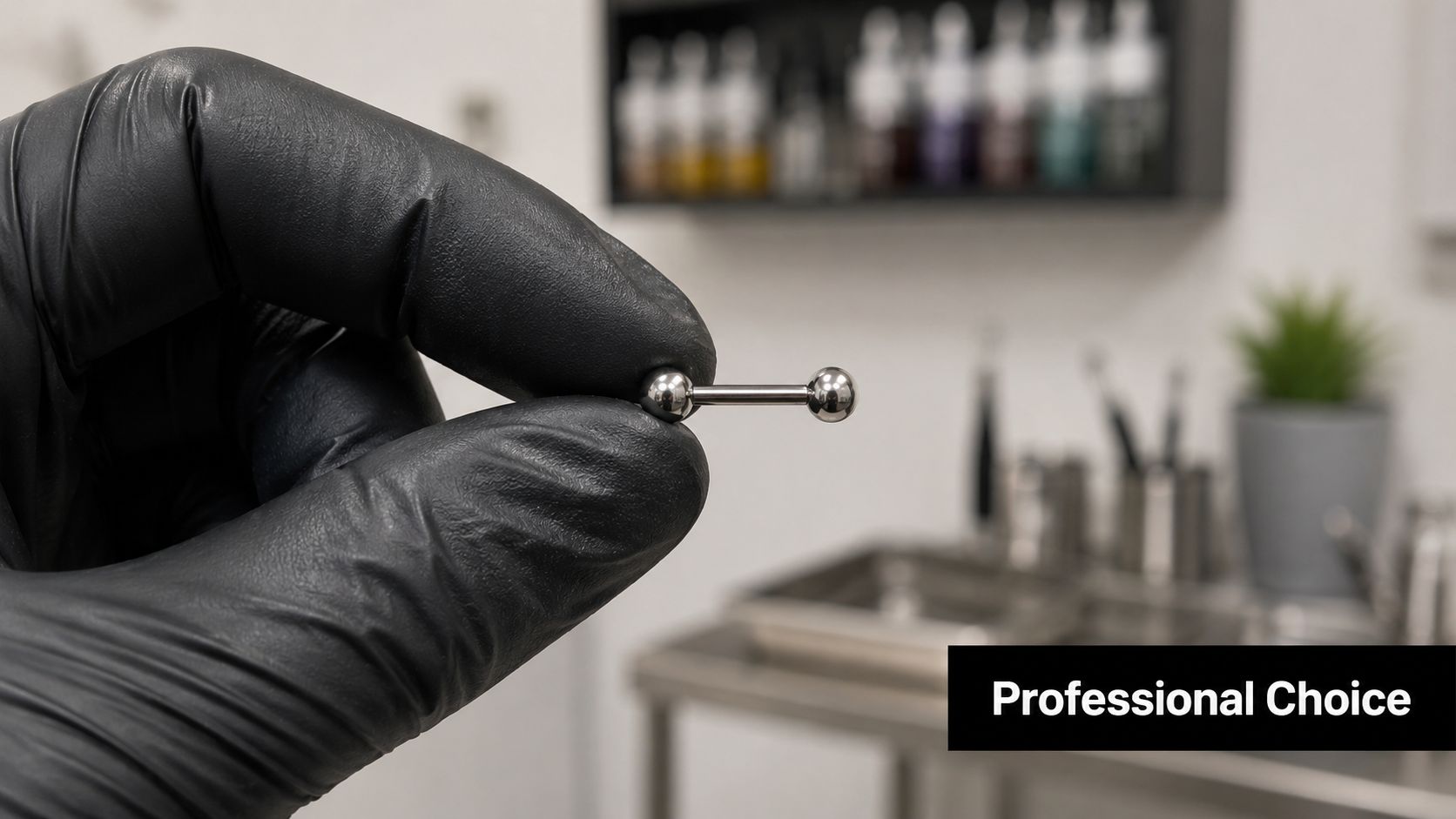 A gloved hand holding a silver barbell piercing jewelry against a blurred studio background.