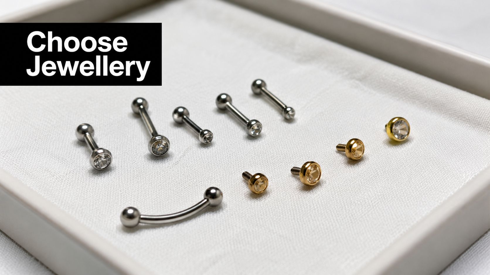A curated selection of silver and gold body piercing jewelry displayed on a white velvet tray.