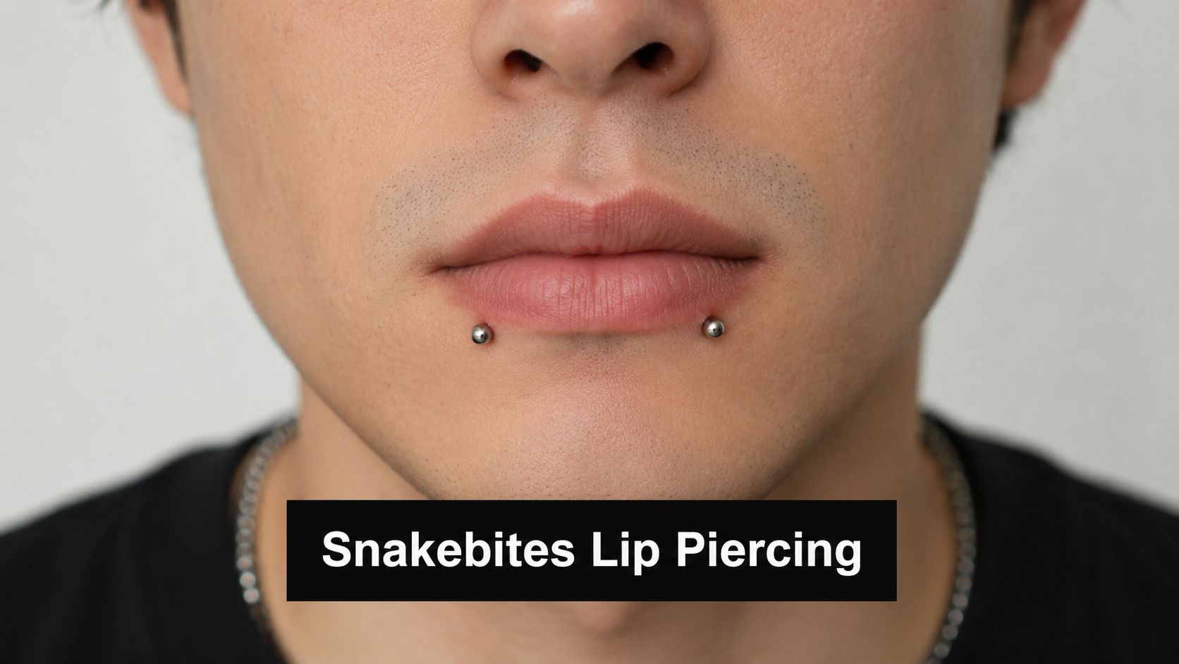 A close-up of a person's lower lip featuring symmetrical silver snakebite piercings on both sides.