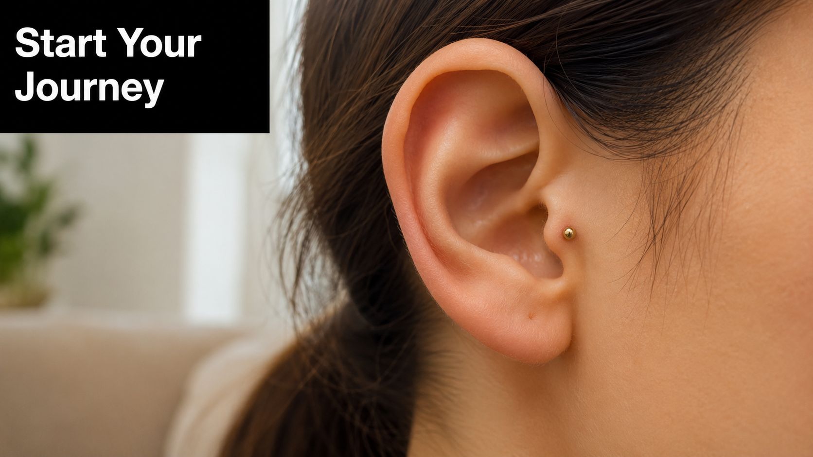 A close-up view of a woman's ear featuring a small gold stud in a tragus piercing.
