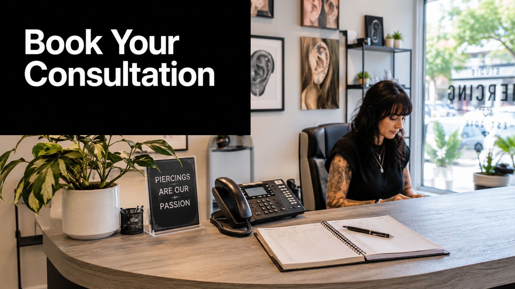 A professional receptionist working at a modern piercing studio counter with booking materials and greenery decor.