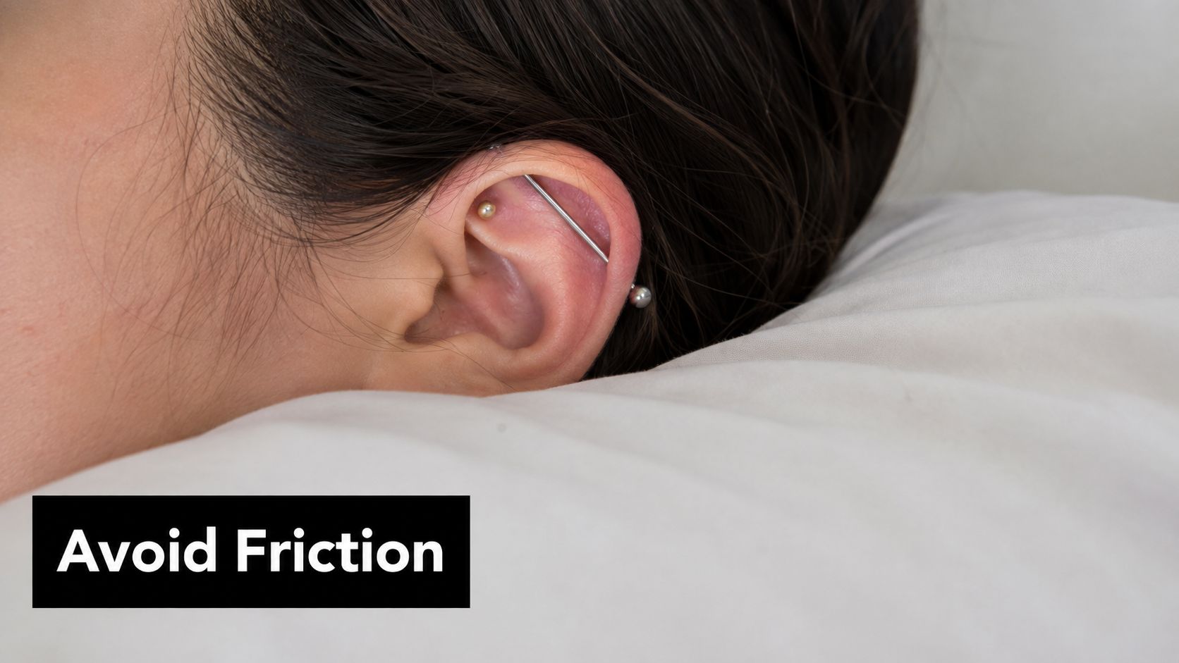 A close-up of a person with an industrial piercing resting their ear on a white pillow.